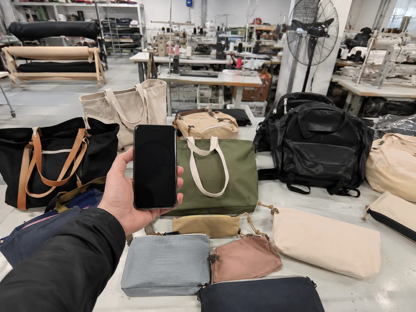 Smartphone-style sourcing desk comparing bag supplier samples, swatches, trims, and quote paperwork