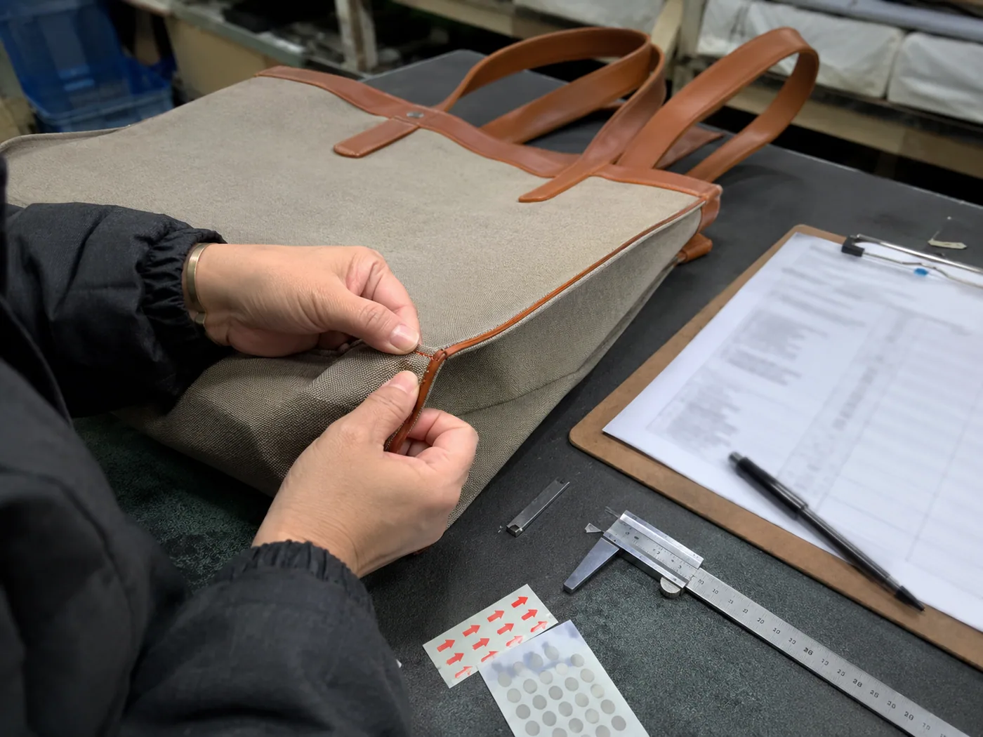 Smartphone-style bag tech pack table with blurred specification sheet, swatches, zipper samples, buckles, and thread cones
