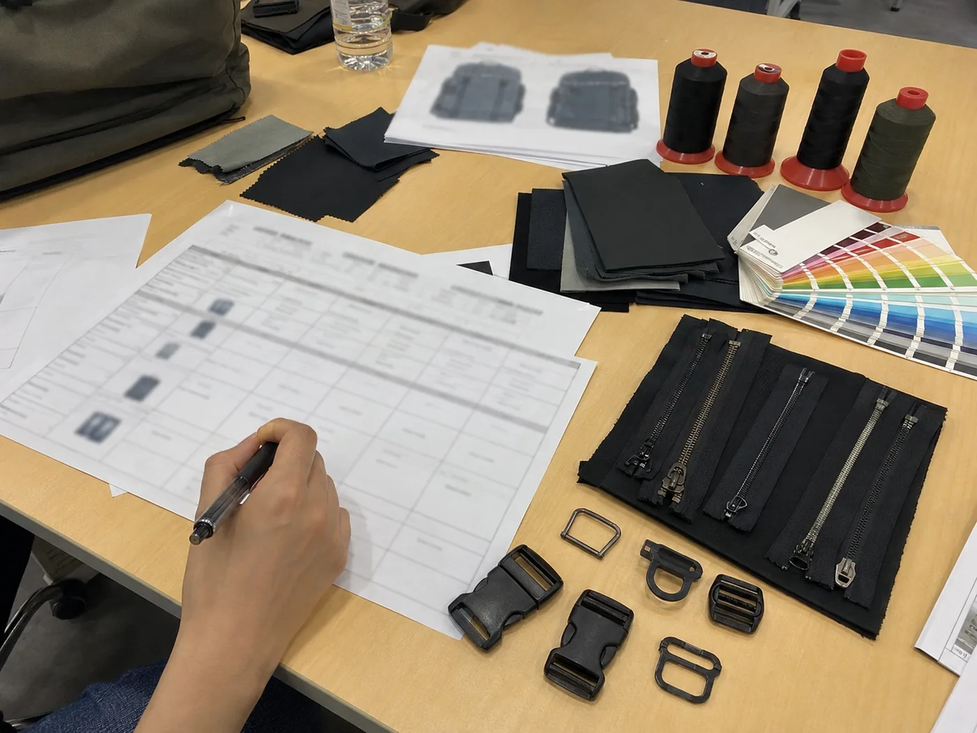 Smartphone-style costing desk for custom bags with swatches, zipper roll, buckle tray, calculator, and sample tote
