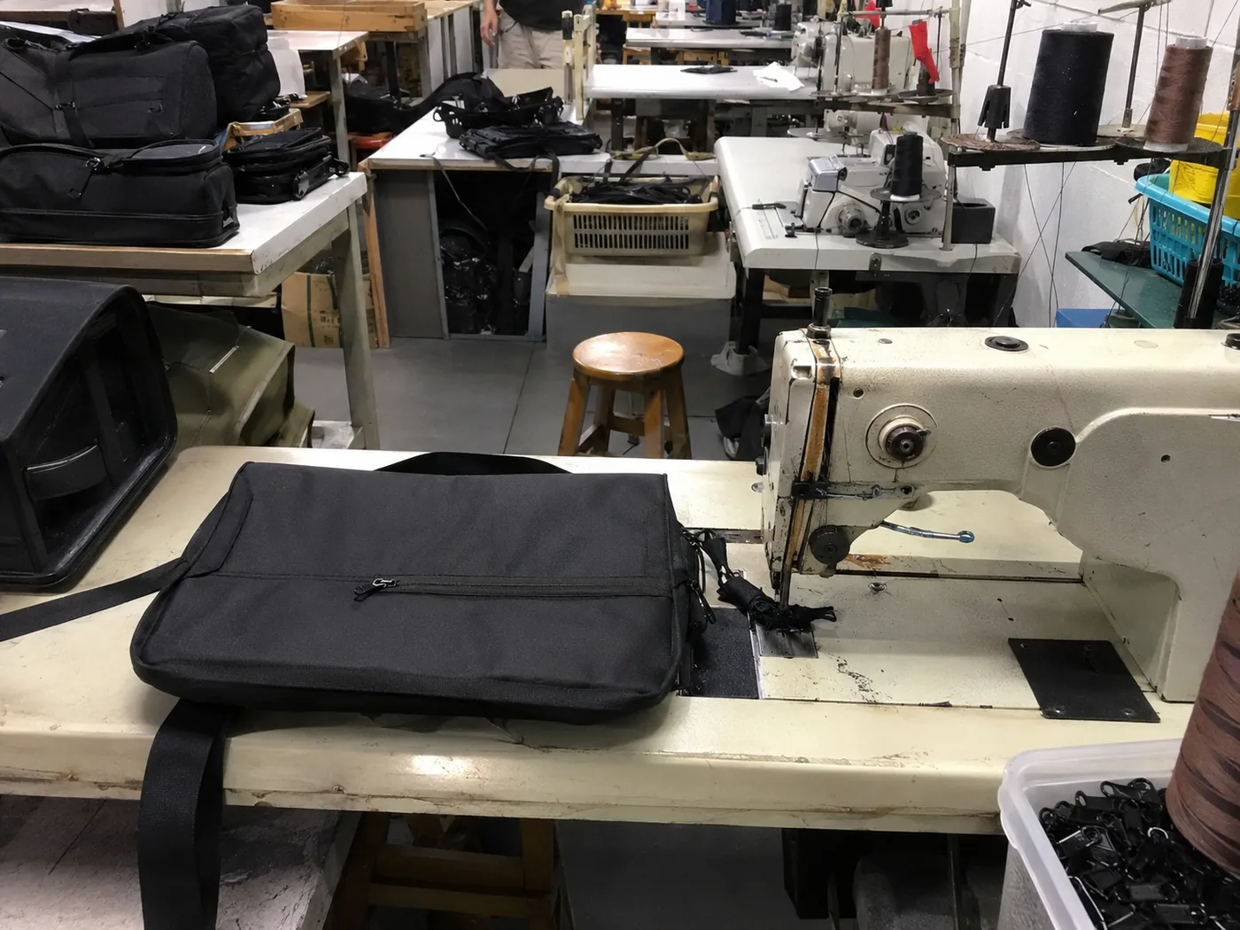 Smartphone-style bag sewing production line with semi-finished totes, thread cones, fabric panels, and worker hands