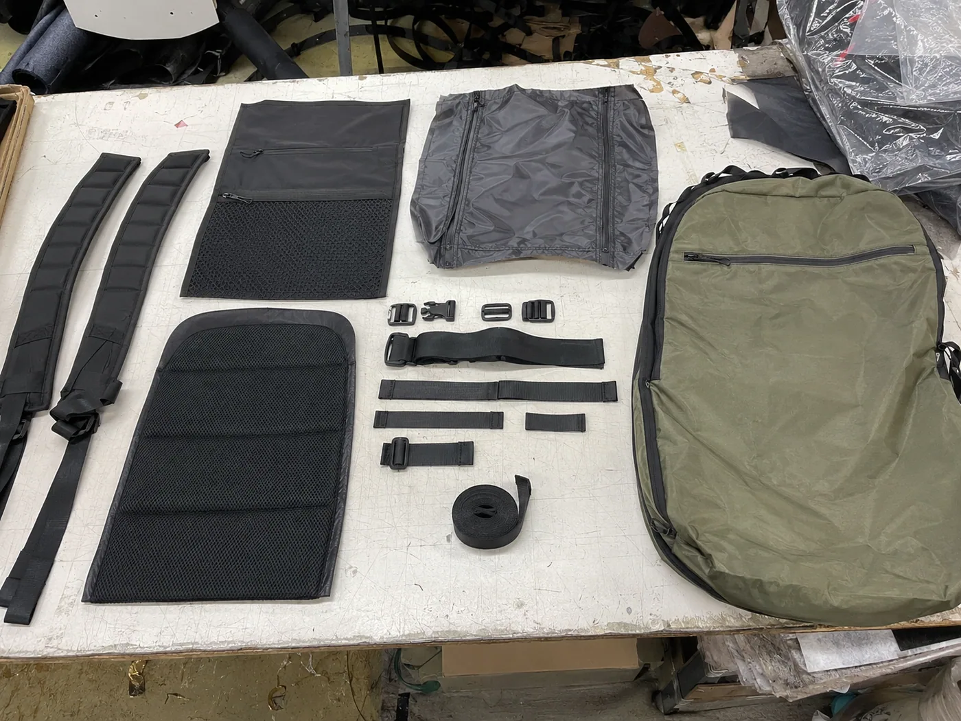 Smartphone-style overhead layout of backpack straps, zipper panel, lining, foam back panel, buckle, webbing, mesh pocket, and shell fabric