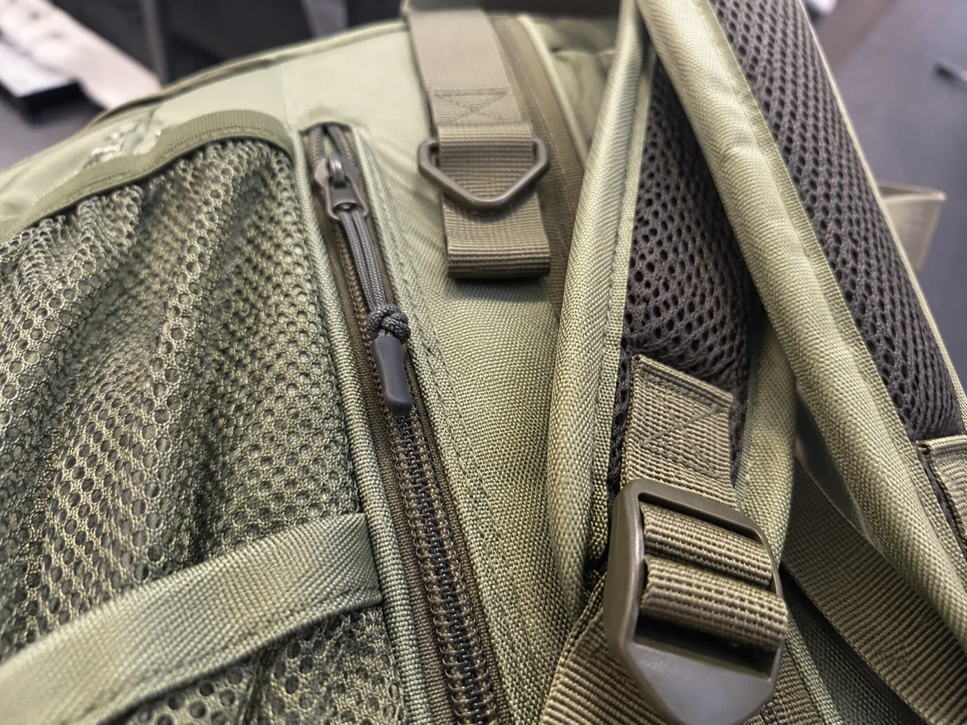 Smartphone-style close-up of backpack strap padding, mesh pocket, zipper teeth, webbing loop, buckle, binding, and stitching