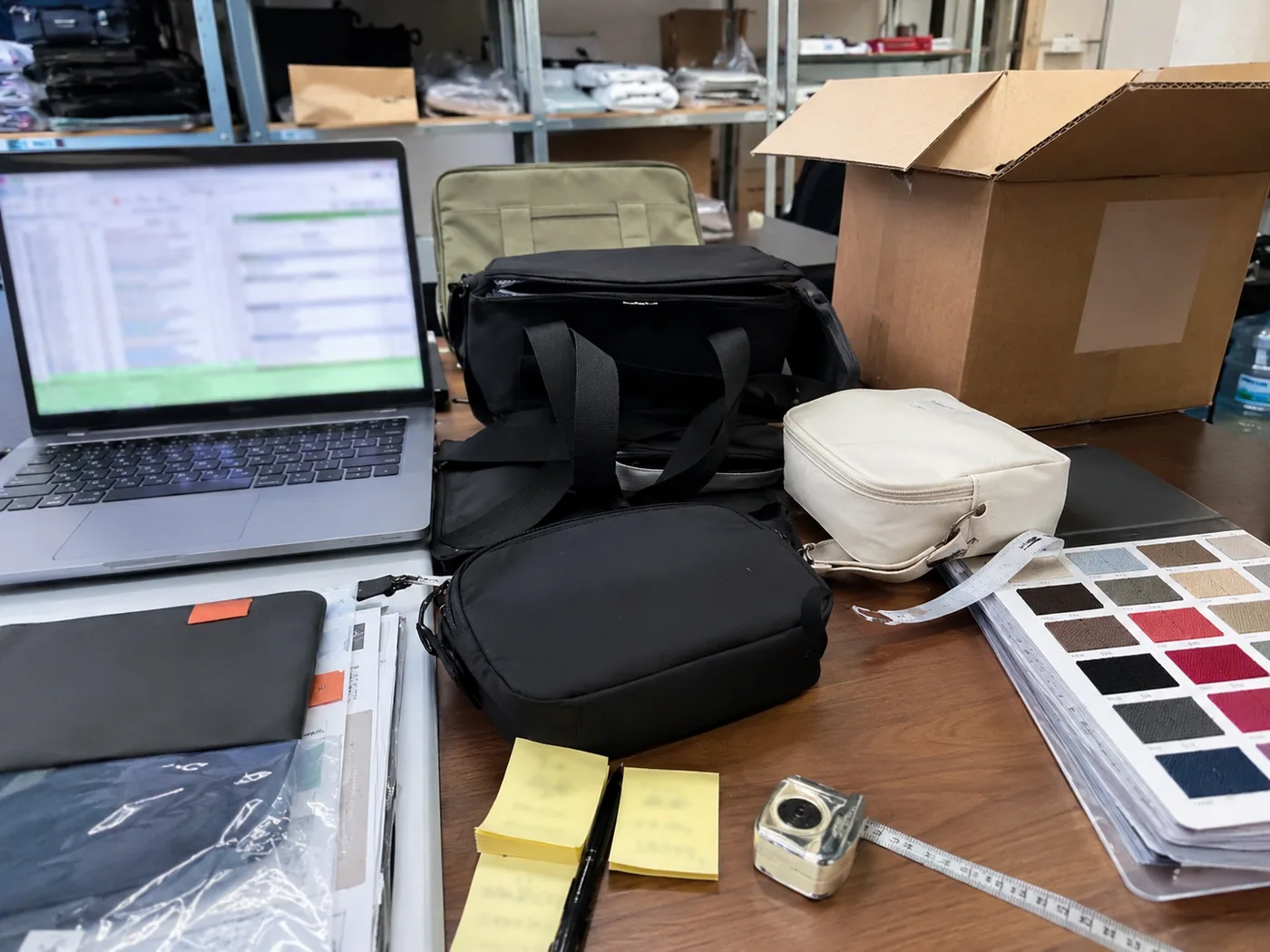 Smartphone-style bag sourcing resource desk with samples, supplier notes, swatches, carton sample, and measuring tape