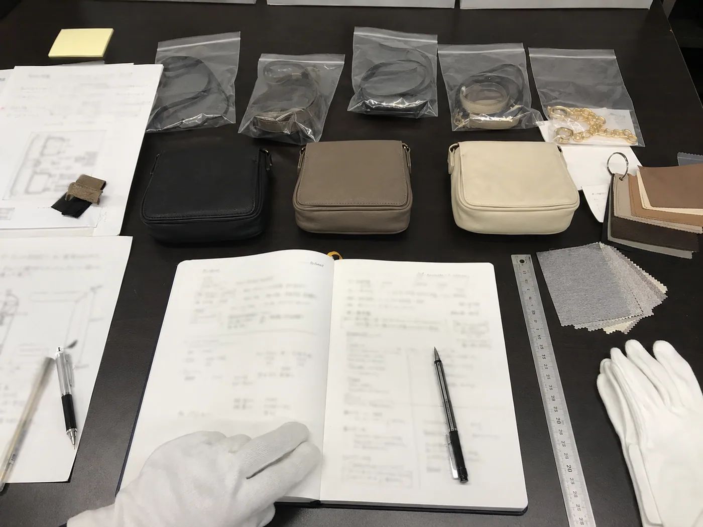 Smartphone-style Japanese buyer review desk with small bag samples, measurements, swatches, blurred notes, ruler, and white gloves